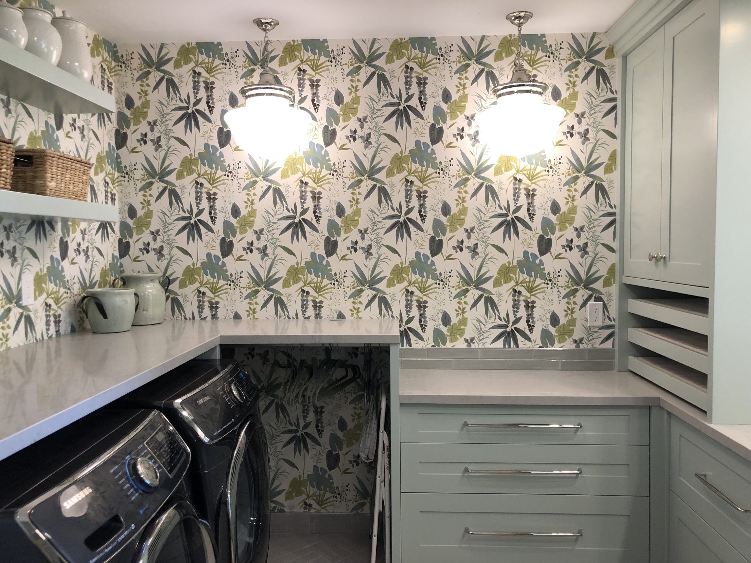 A spacious laundry room in light green tones with leaf wallpaper.