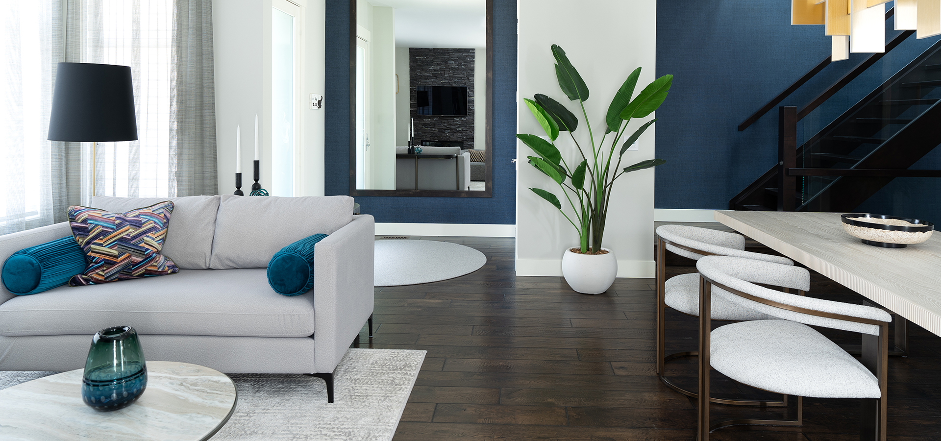 A modern living room with light grey furniture and blue accents on a dark hardwood floor.