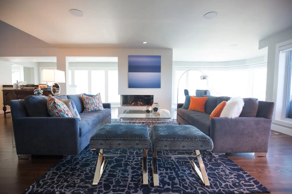 Modern custom living room furniture including two low back blue sofas facing each other across a glass-topped coffee table and two plush covered stools.