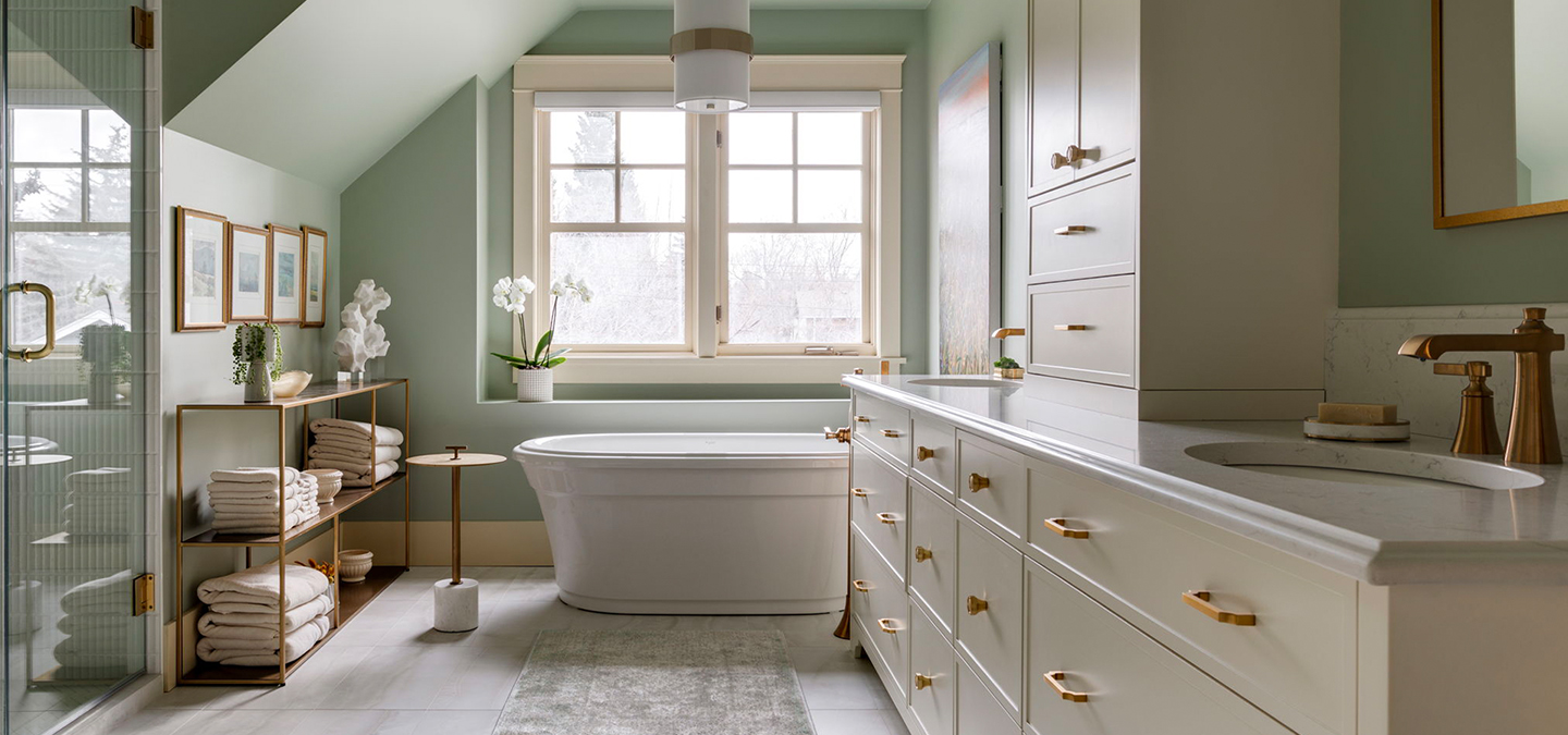 A newly renovated bathroom with light green walls, cream cabinetry, a large soaker tub and copper fixtures.