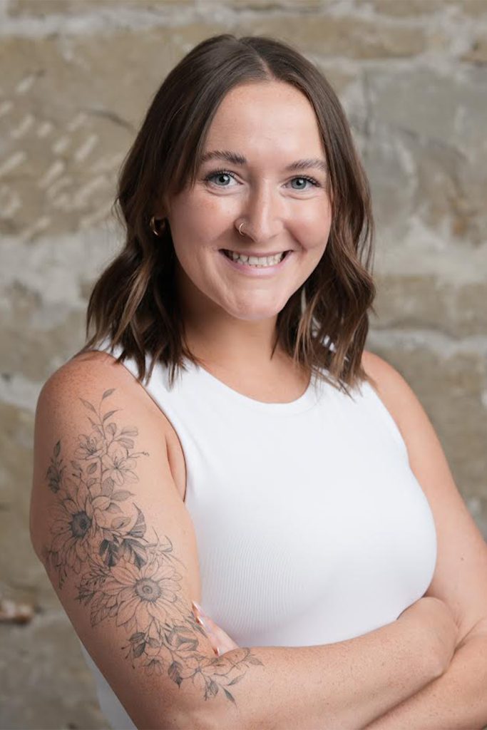 A professional headshot of a woman standing in front of a patterned background, smiling confidently.