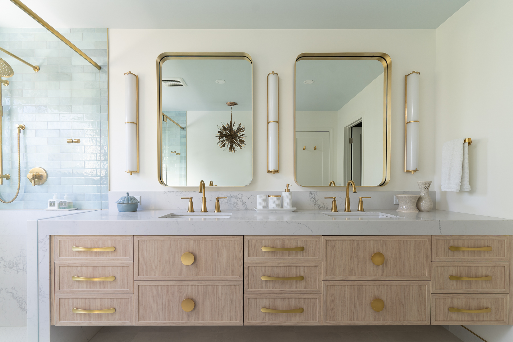 A modern bathroom renovation with 2 sinks and gold fixtures.