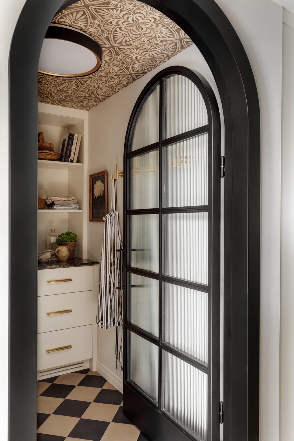 A black arched designer door opening into a new kitchen pantry.