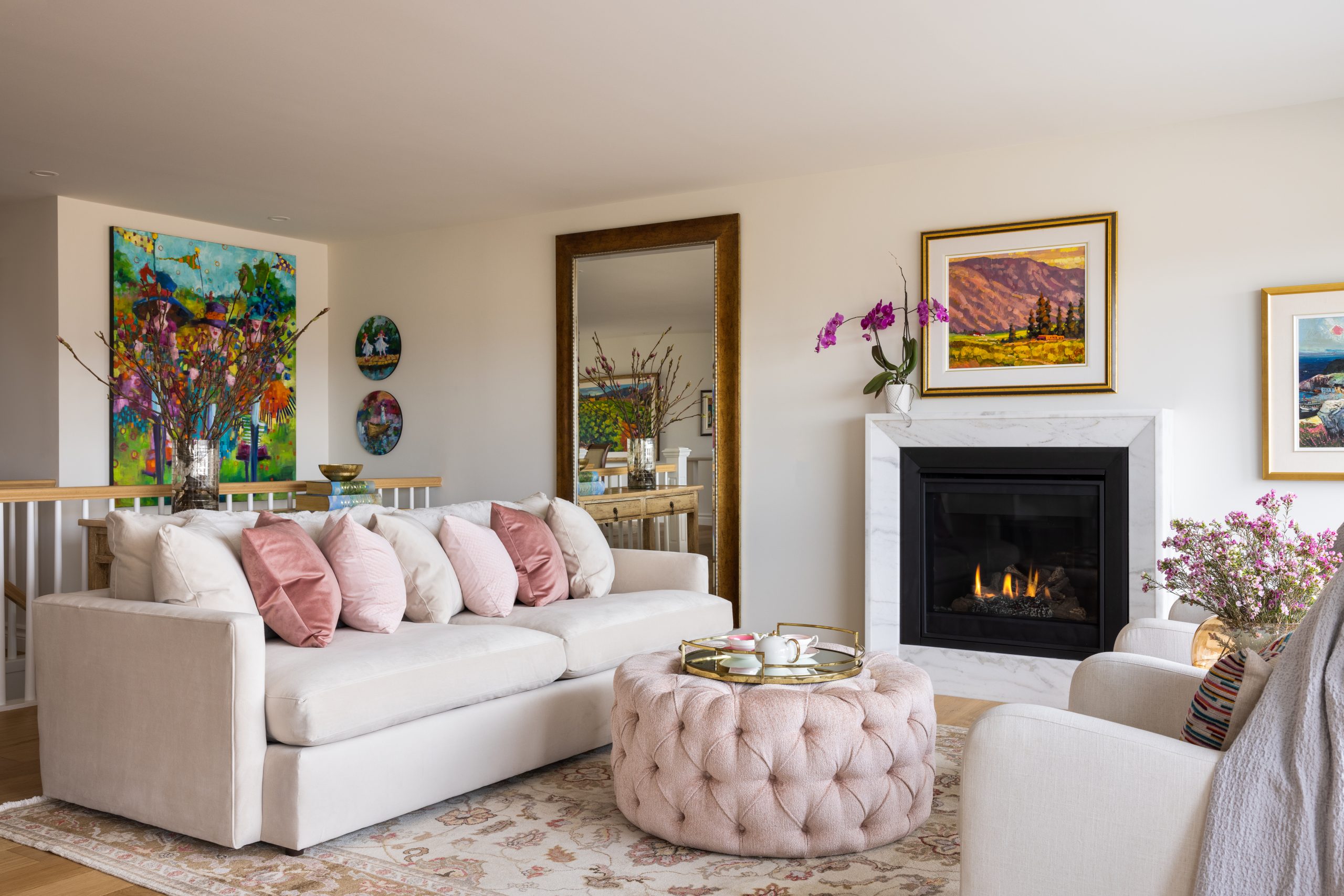 A living room with a cream sofa, a large round plush pink ottoman and pink accent pillows.